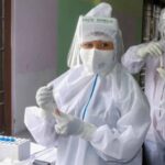 Health workers wearing PPE hold samples for COVID-19 rapid antigen testing.
