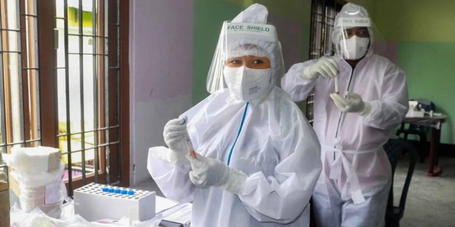 Health workers wearing PPE hold samples for COVID-19 rapid antigen testing.