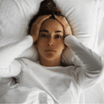 Tired woman relaxing on bed with eyes closed after a long week, embracing mindful rest.