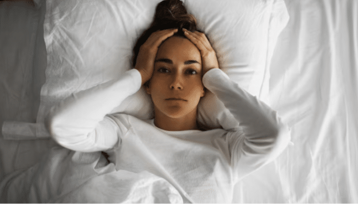 Tired woman relaxing on bed with eyes closed after a long week, embracing mindful rest.